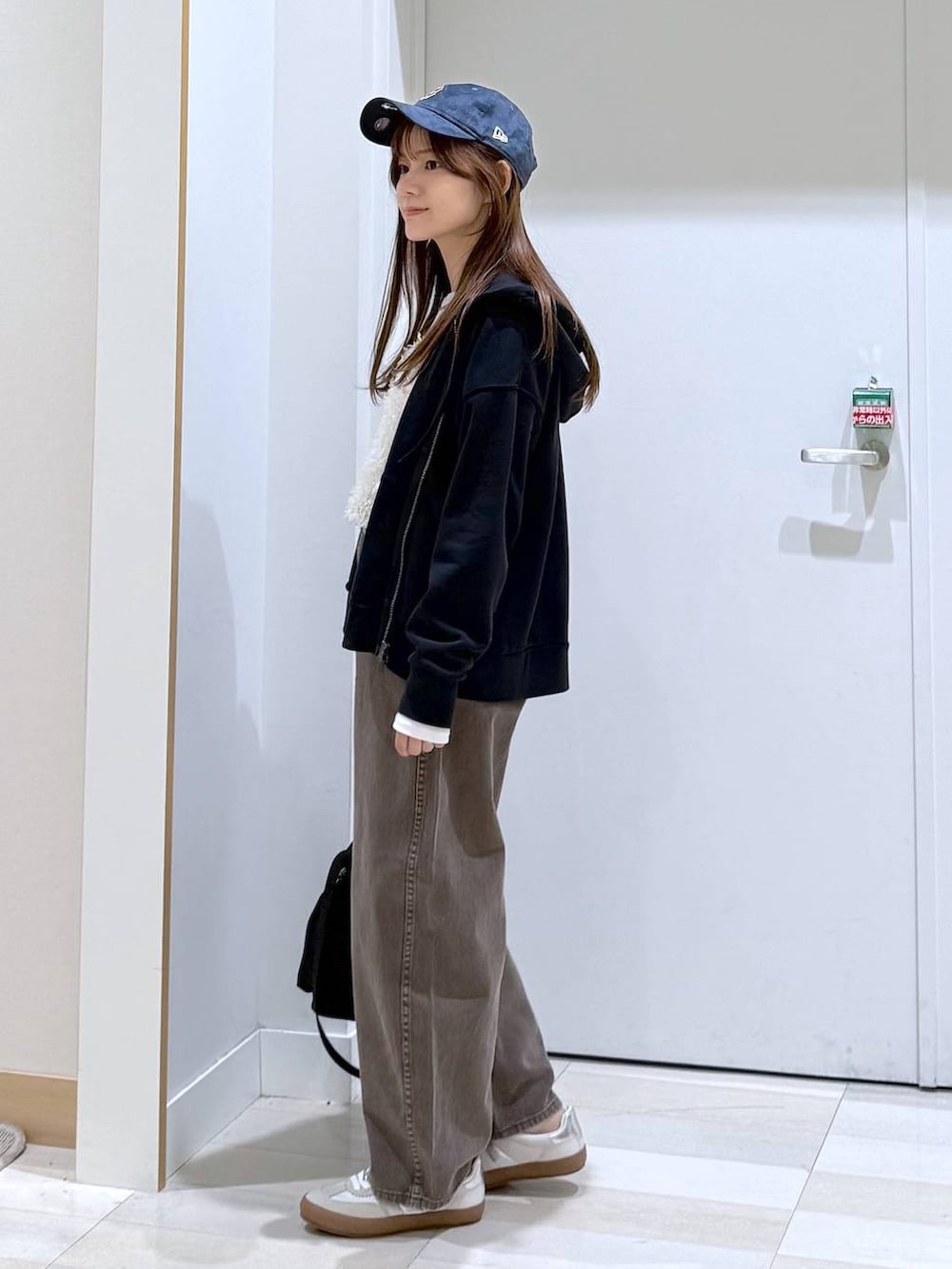 ホワイト系のスニーカー、ブラック系のショルダーバッグ、ブラウン系のデニムパンツを着用したレディースの冬コーディネートの2枚目の写真