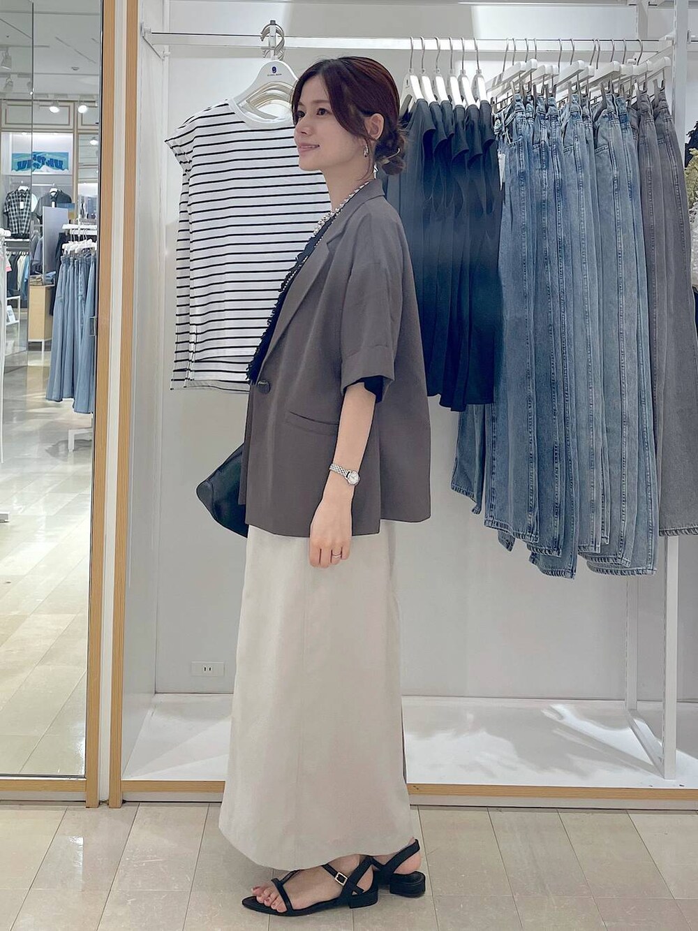 ブラック系のショルダーバッグ、グレー系のスカート、ブラック系のサンダルを着用したレディースの夏コーディネートの2枚目の写真