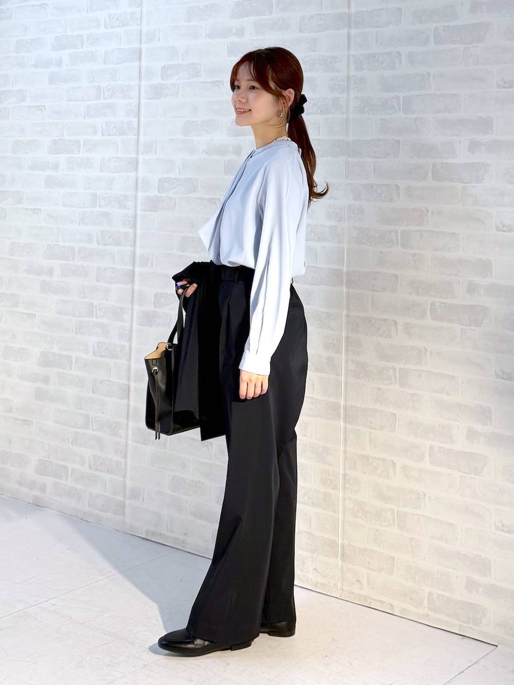 ブラック系のローファー、ブラック系のショルダーバッグ、ブルー系のスラックスを着用したレディースの冬コーディネートの2枚目の写真