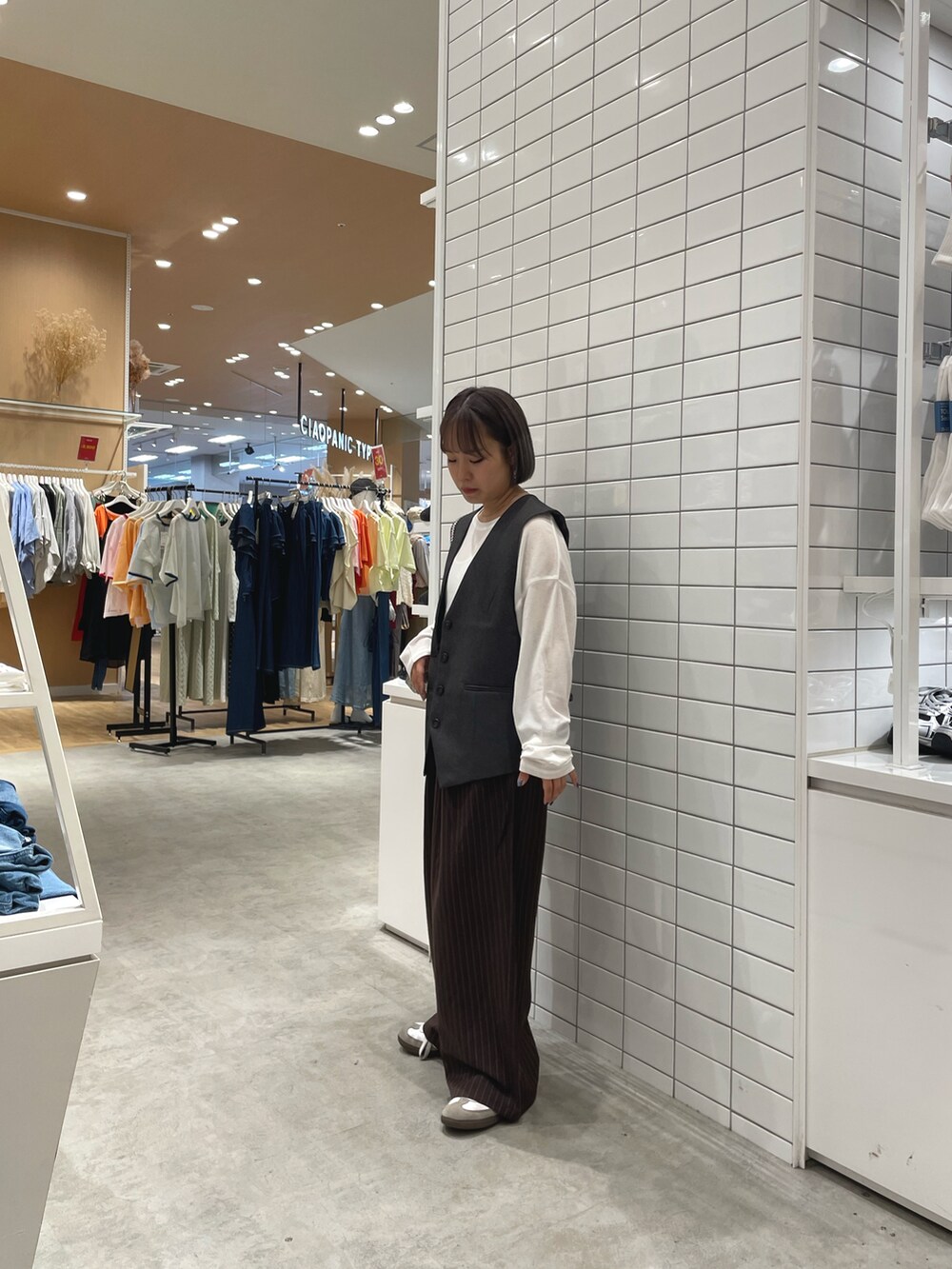 ゴールド系のショルダーバッグ、ブラウン系のスラックス、ホワイト系のTシャツ/カットソーを着用したレディースの秋コーディネートの2枚目の写真