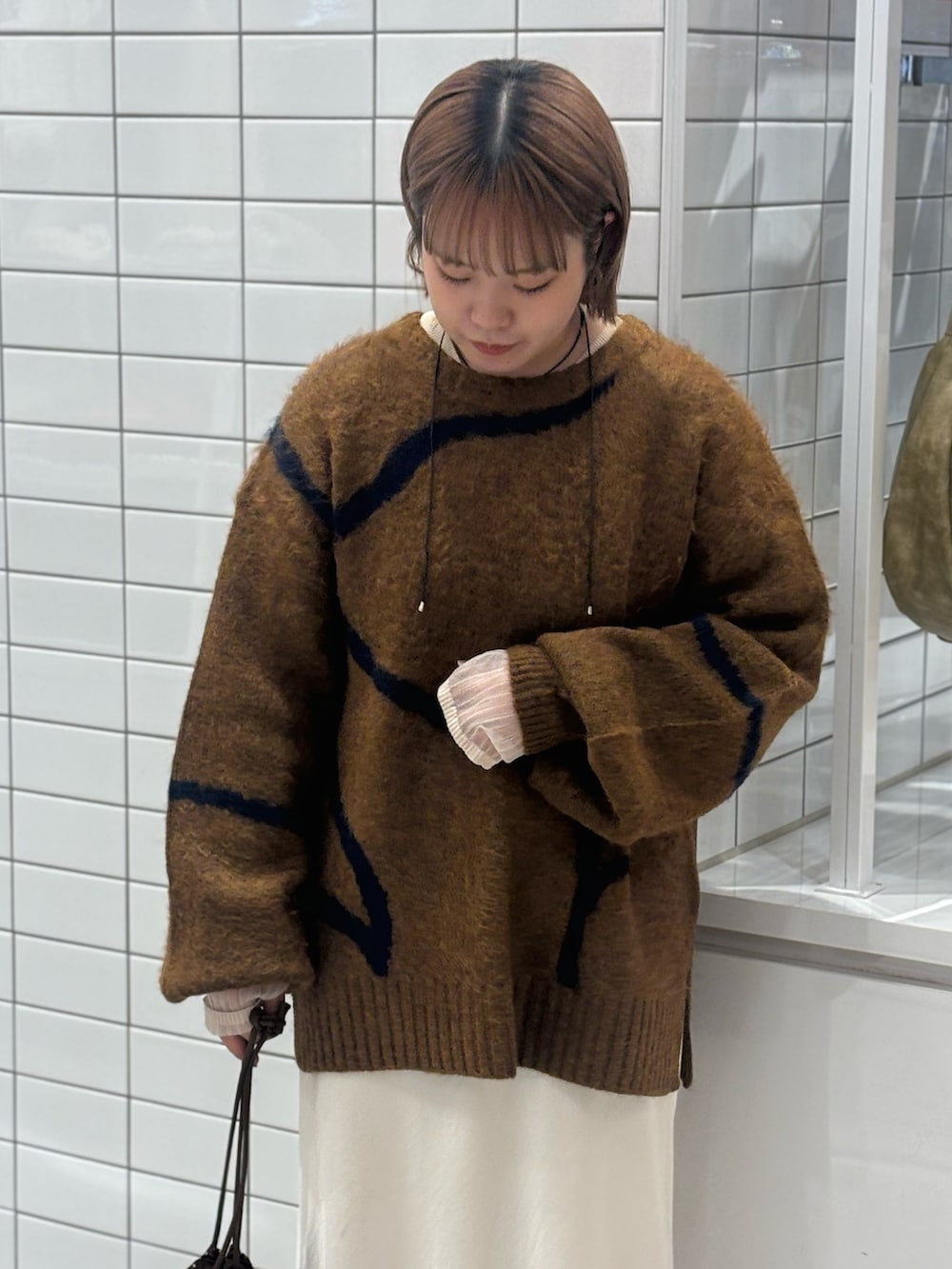 ブラウン系のニット/セーター、ホワイト系のスカート、ブラウン系のショルダーバッグを着用したレディースの冬コーディネートの4枚目の写真