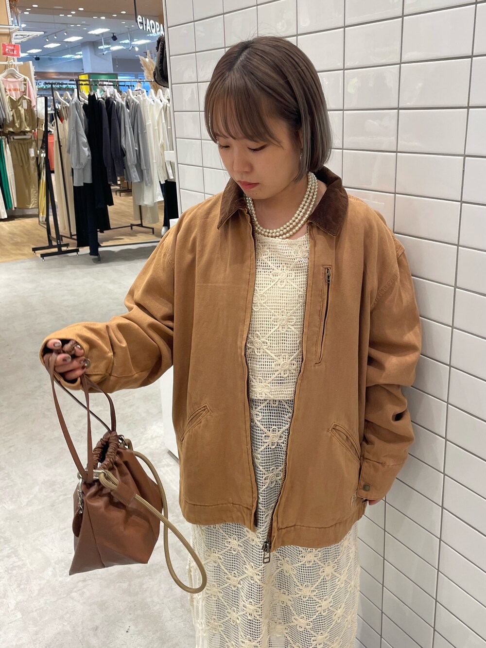 ホワイト系のワンピース、ブラウン系のショルダーバッグ、ブルー系のデニムパンツを着用したレディースの秋コーディネートの4枚目の写真