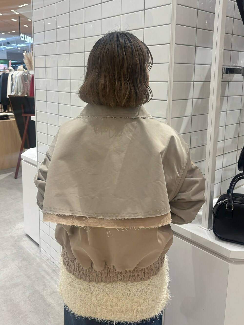 ベージュ系のトレンチコート、ブラック系のショルダーバッグ、ブルー系のデニムパンツを着用したレディースの春コーディネートの3枚目の写真
