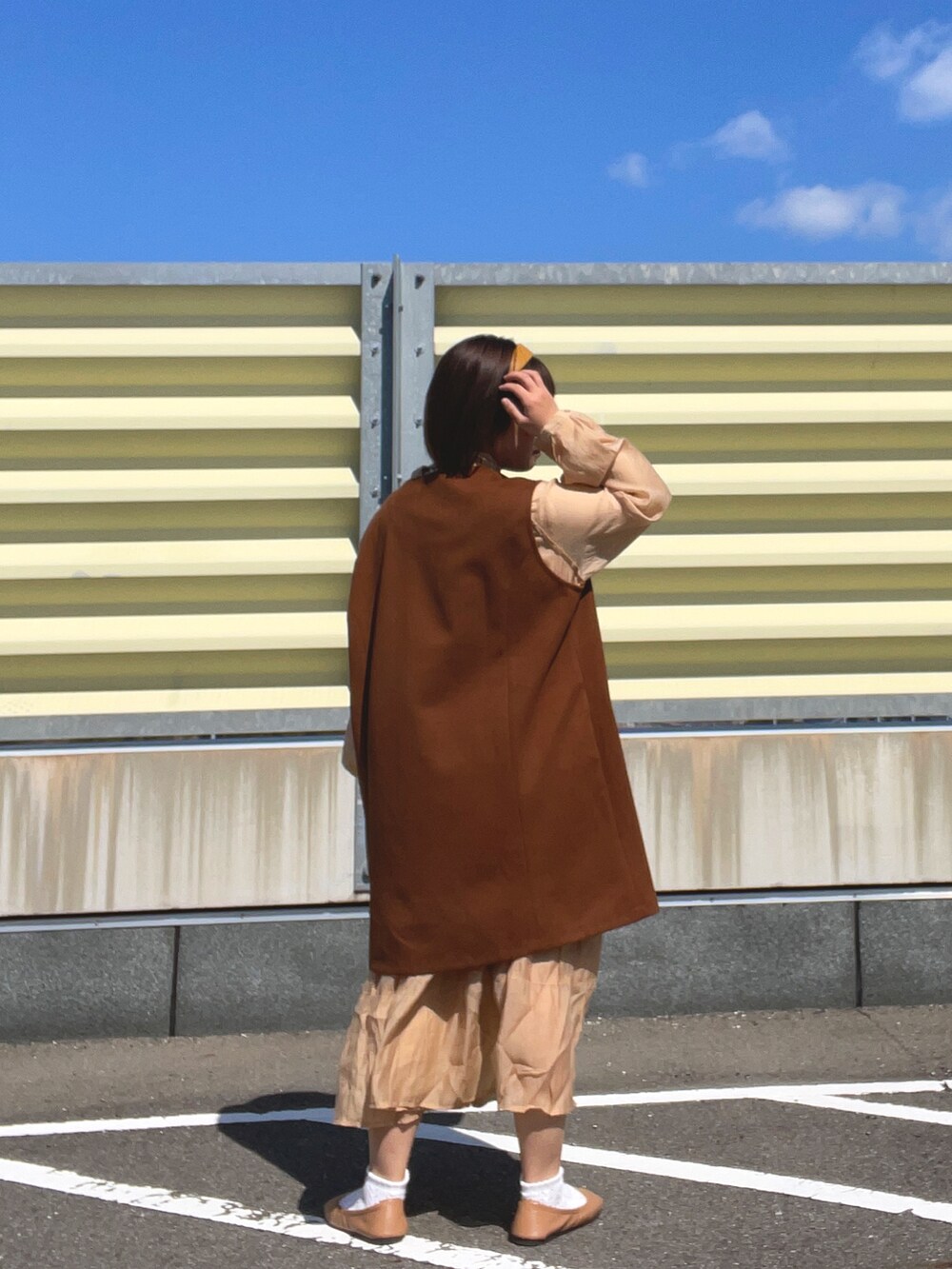 オレンジ系のワンピース、ブラウン系のベスト、ブラウン系のパンプスを着用したレディースの春コーディネートの4枚目の写真