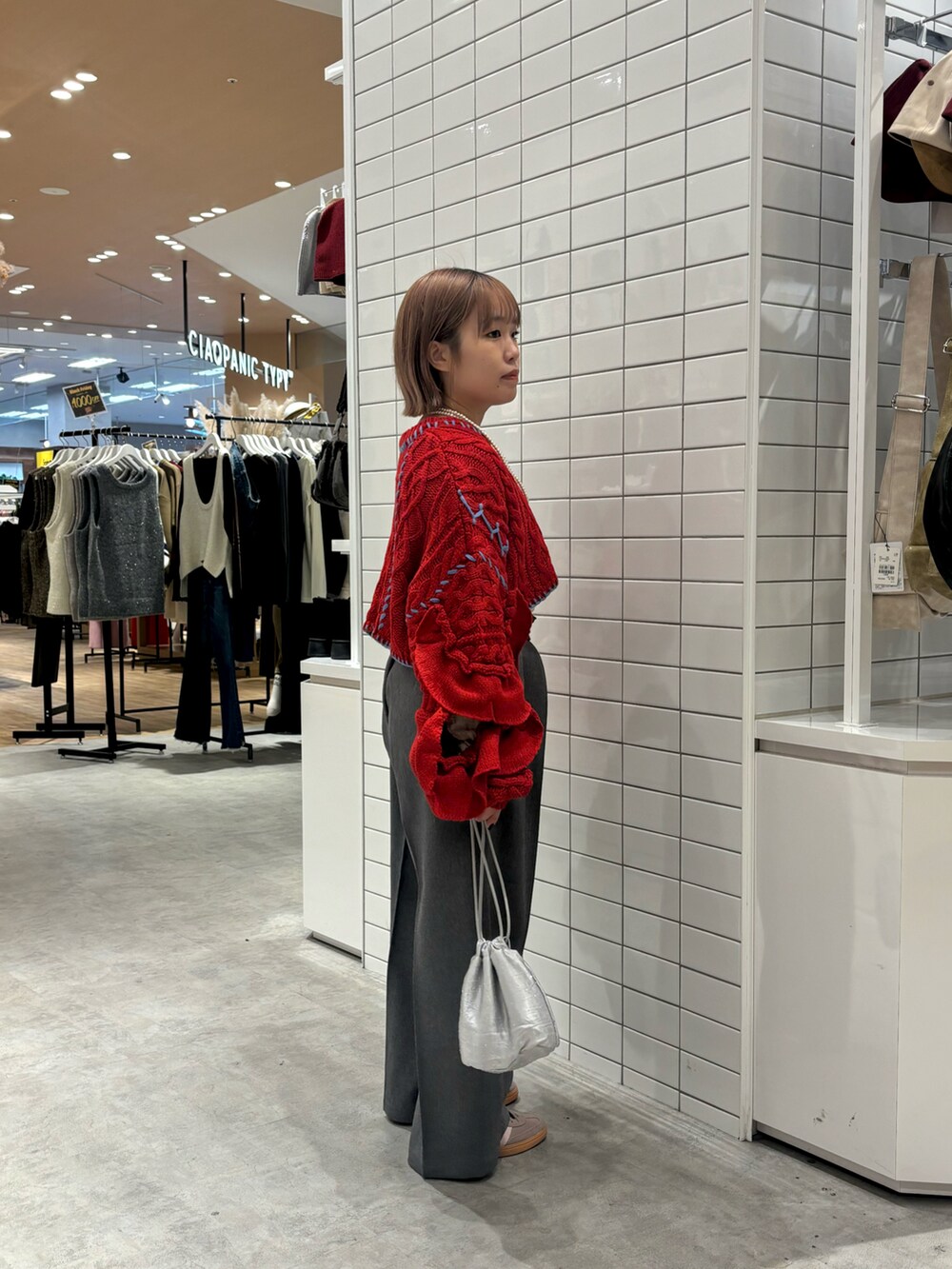 レッド系のニット/セーター、グレー系のスラックス、シルバー系のトートバッグを着用したレディースの冬コーディネートの3枚目の写真