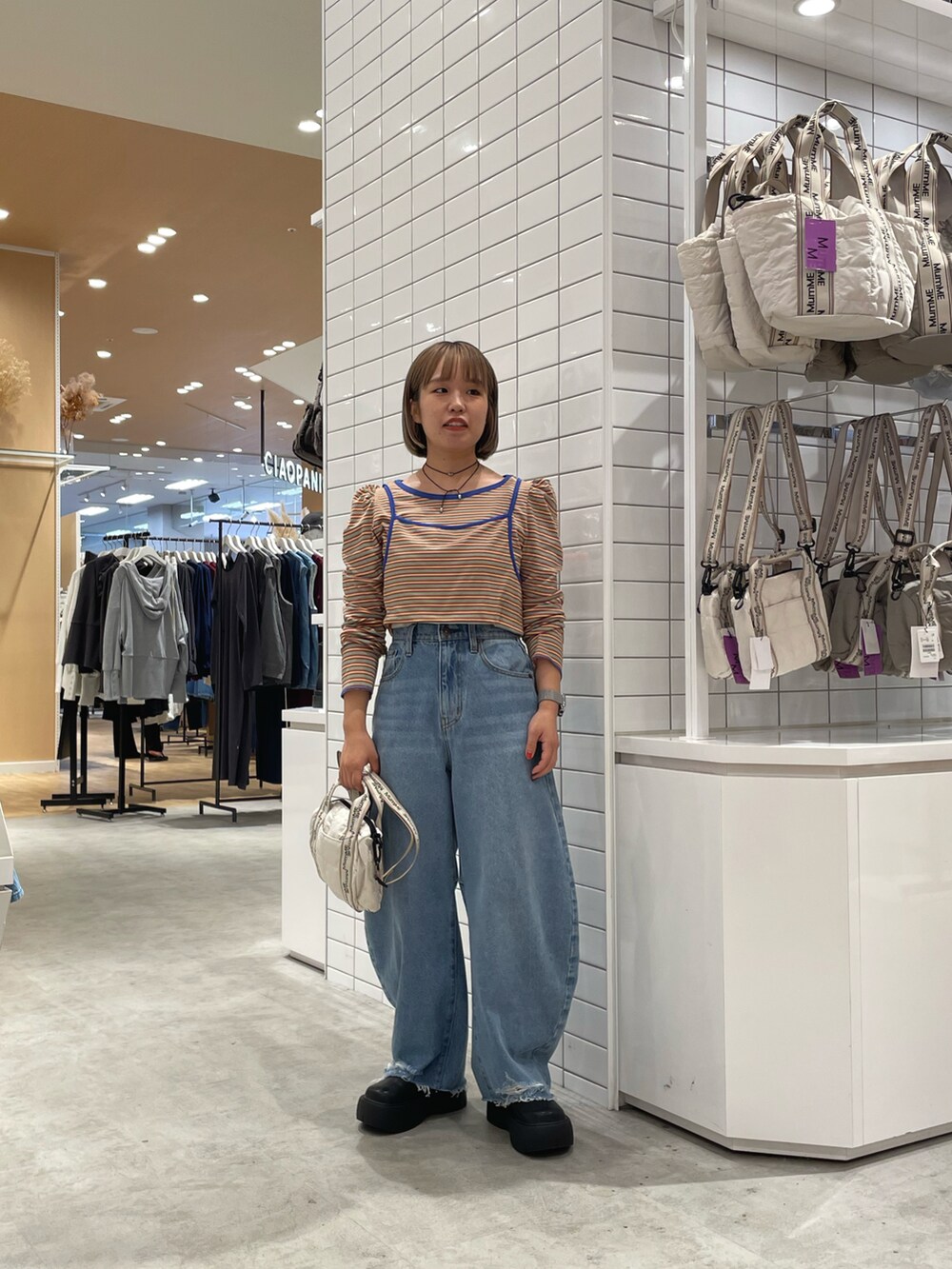 ブルー系のデニムパンツ、ブラック系のブーツ、ホワイト系のショルダーバッグを着用したレディースの秋コーディネートの2枚目の写真