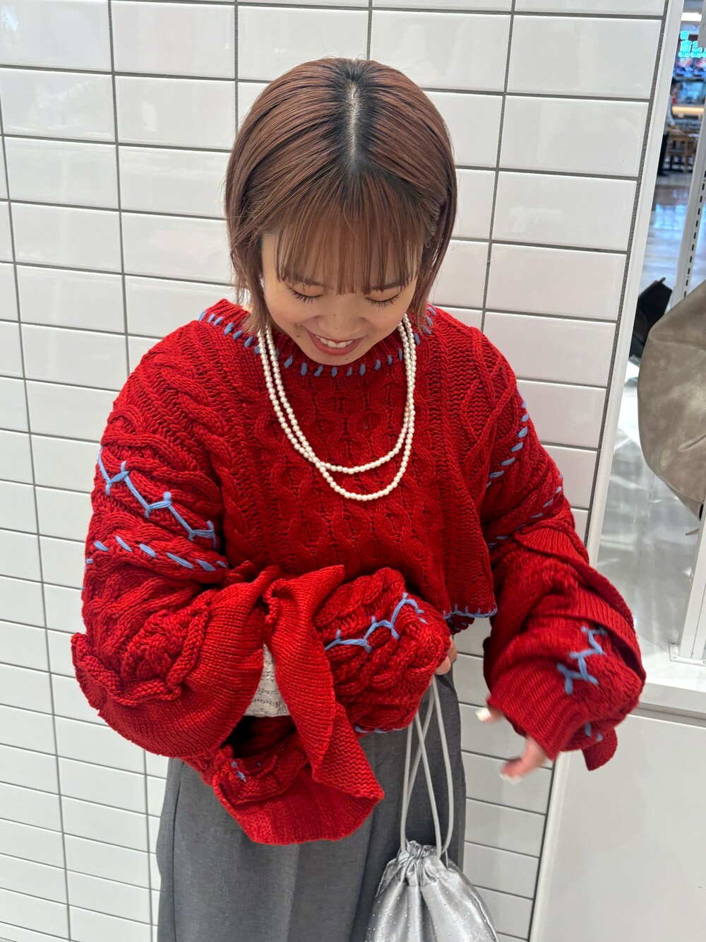 レッド系のニット/セーター、グレー系のスラックス、シルバー系のトートバッグを着用したレディースの冬コーディネートの4枚目の写真