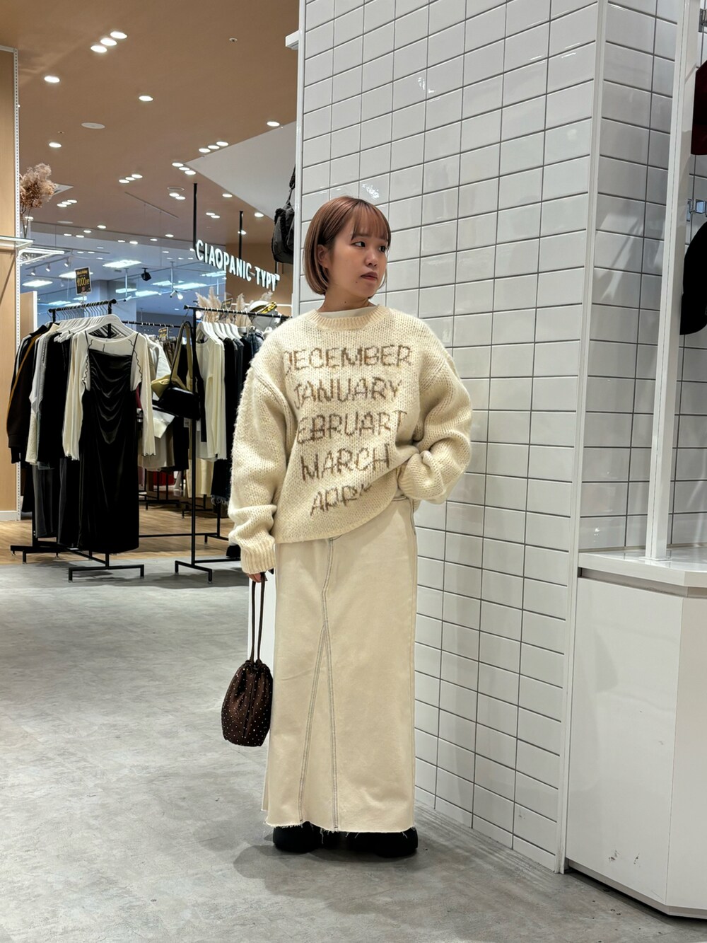 ベージュ系のニット/セーター、ホワイト系のデニムスカート、ブラウン系のショルダーバッグを着用したレディースの秋コーディネートの2枚目の写真