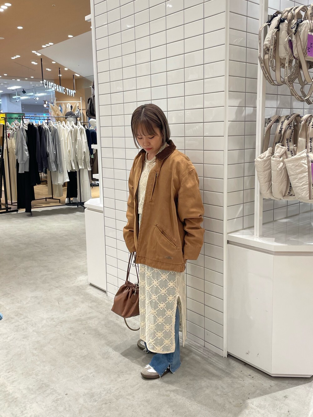 ホワイト系のワンピース、ブラウン系のショルダーバッグ、ブルー系のデニムパンツを着用したレディースの秋コーディネートの2枚目の写真