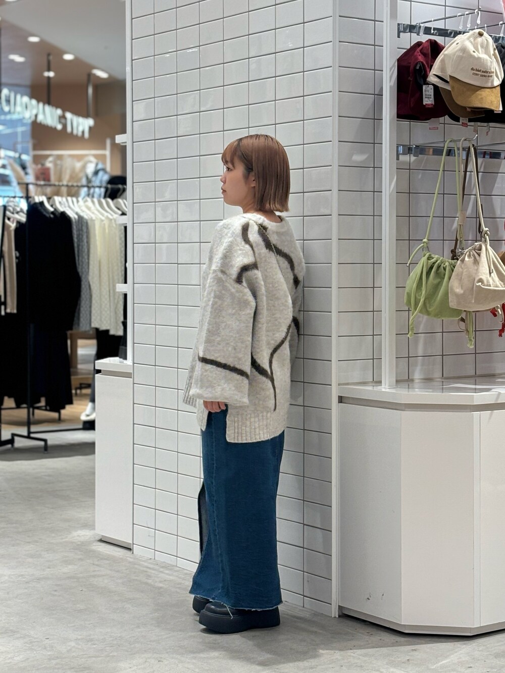 ホワイト系のニット/セーター、ブルー系のデニムスカート、ブラック系のブーツを着用したレディースの冬コーディネートの2枚目の写真