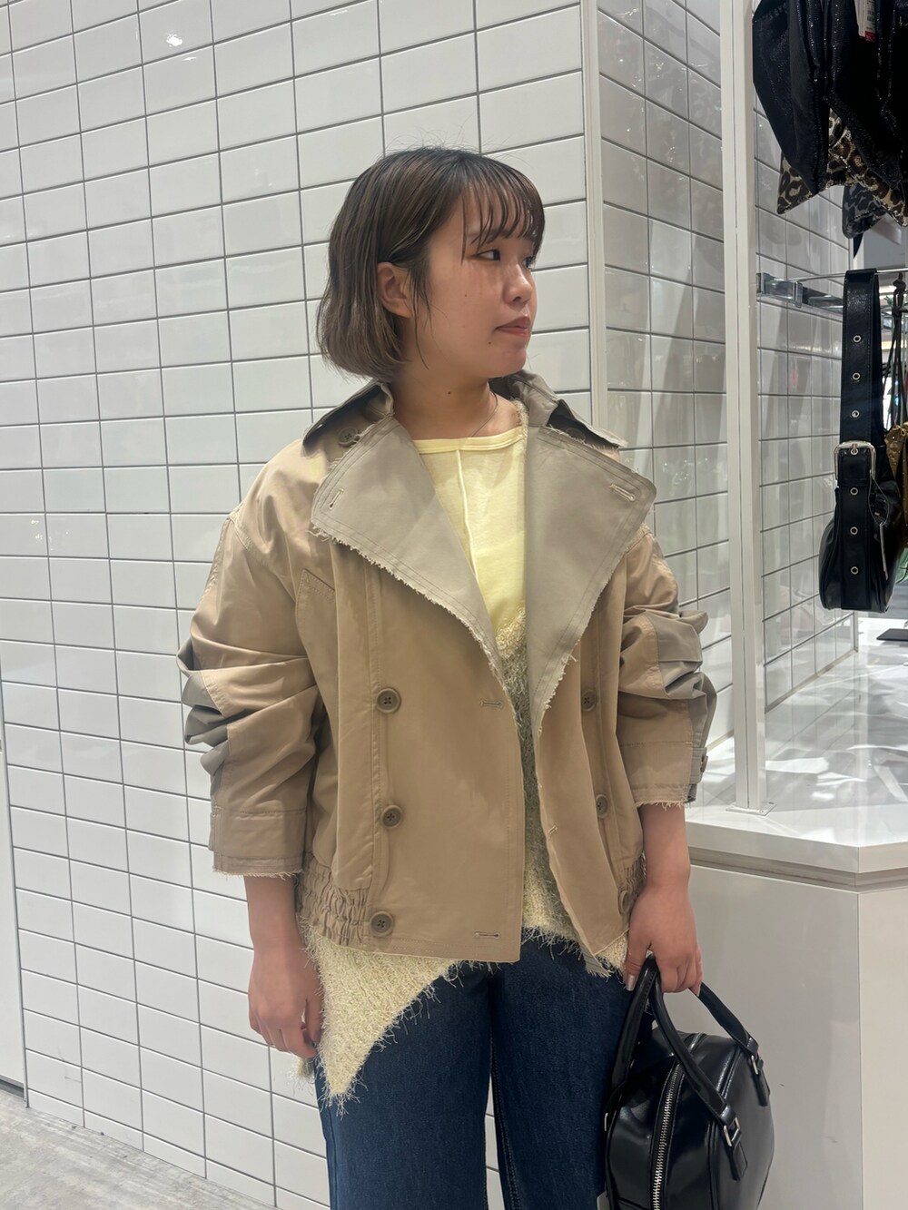 ベージュ系のトレンチコート、ブラック系のショルダーバッグ、ブルー系のデニムパンツを着用したレディースの春コーディネートの2枚目の写真