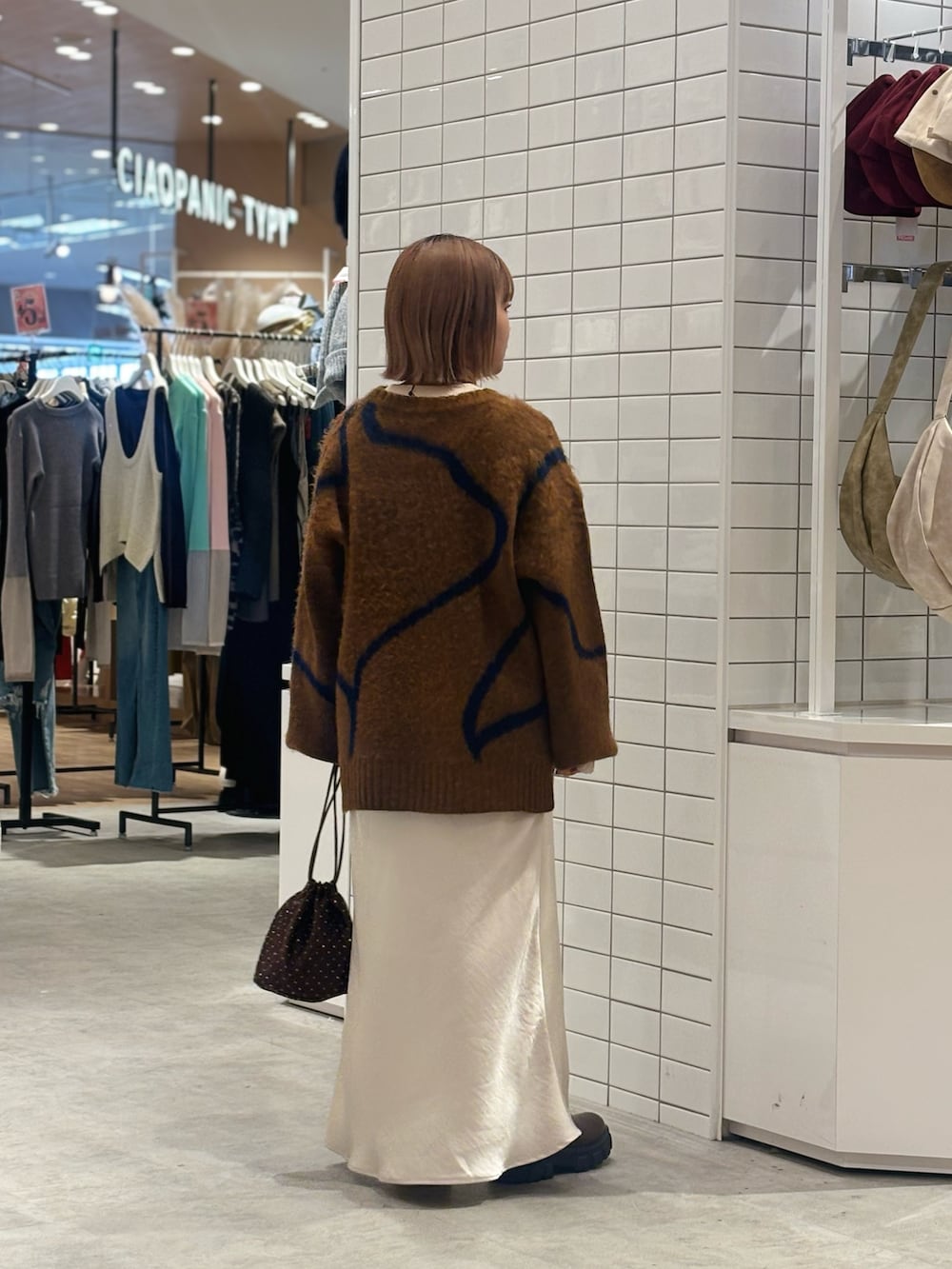 ブラウン系のニット/セーター、ホワイト系のスカート、ブラウン系のショルダーバッグを着用したレディースの冬コーディネートの3枚目の写真