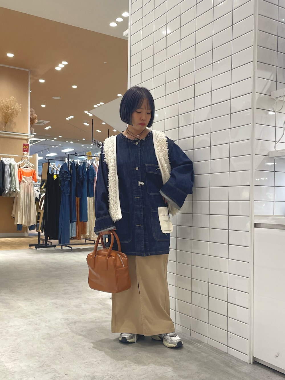 ホワイト系のスニーカー、ホワイト系のベスト、ブルー系のデニムジャケットを着用したレディースの秋コーディネートの2枚目の写真