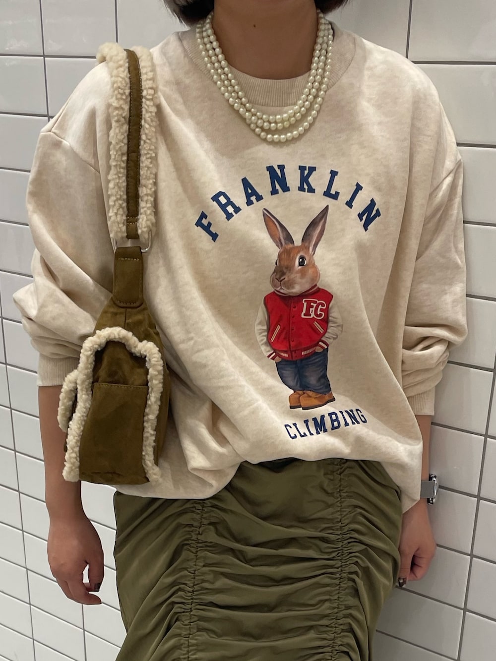 ホワイト系のスウェット、ブラウン系のショルダーバッグ、グリーン系のスカートを着用したレディースの秋コーディネートの3枚目の写真