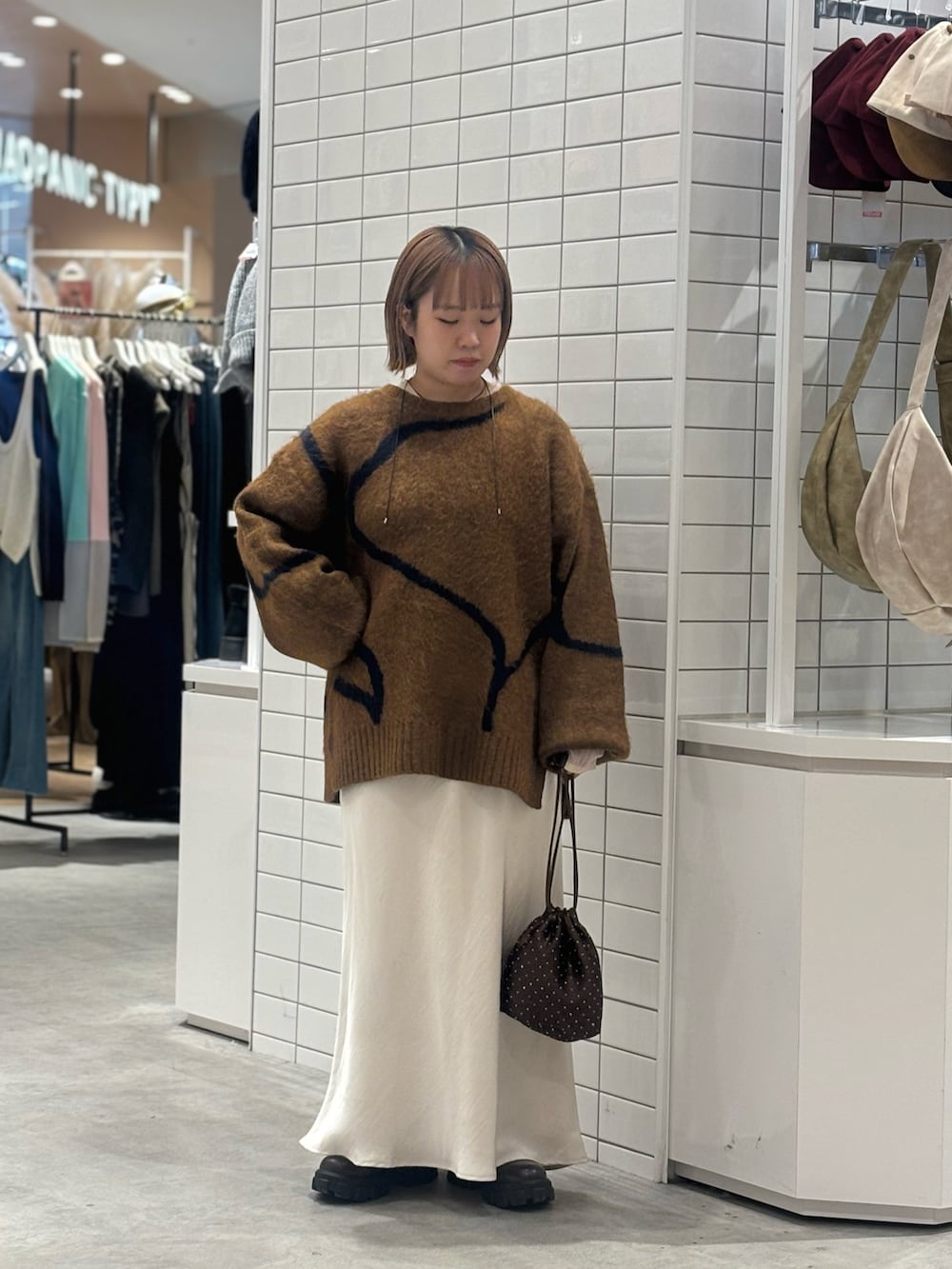 ブラウン系のニット/セーター、ホワイト系のスカート、ブラウン系のショルダーバッグを着用したレディースの冬コーディネートの2枚目の写真