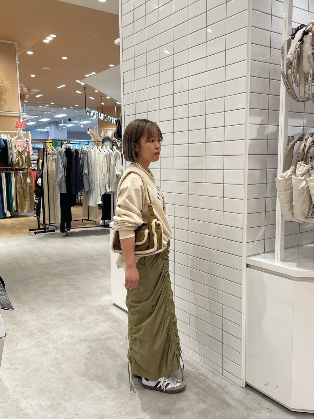 ホワイト系のスウェット、ブラウン系のショルダーバッグ、グリーン系のスカートを着用したレディースの秋コーディネートの2枚目の写真