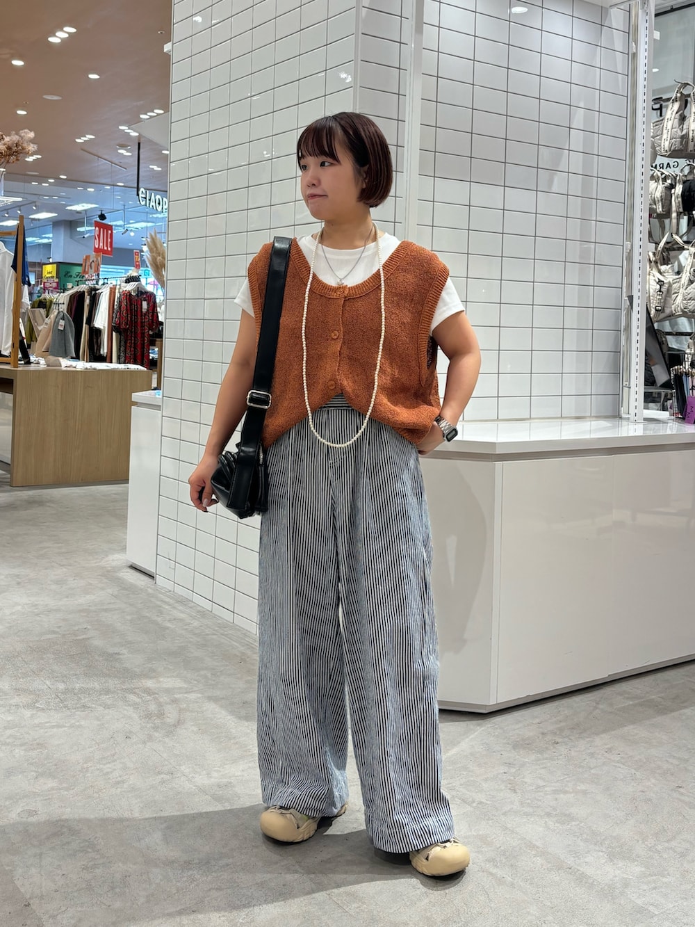 オレンジ系のベスト、ブラック系のショルダーバッグ、ブルー系のデニムパンツを着用したレディースの夏コーディネートの2枚目の写真