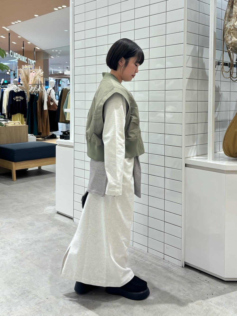 グリーン系のベスト、ブラック系のショルダーバッグ、ブラック系のサンダルを着用したレディースの春コーディネートの2枚目の写真