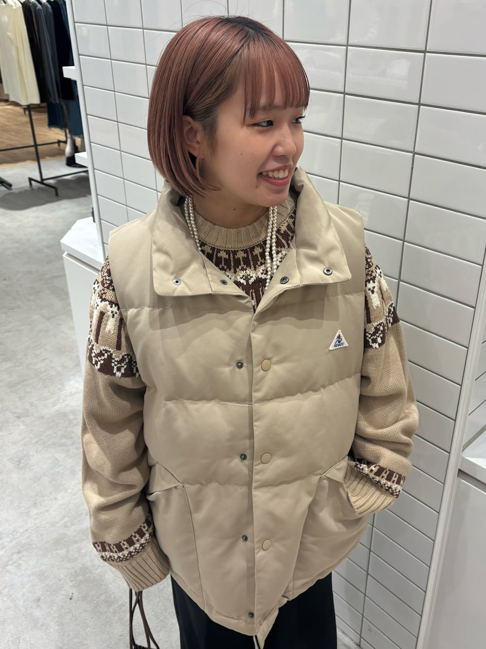 ブラック系のスラックス、ブラウン系のショルダーバッグ、ベージュ系のダウンベストを着用したレディースの冬コーディネートの2枚目の写真