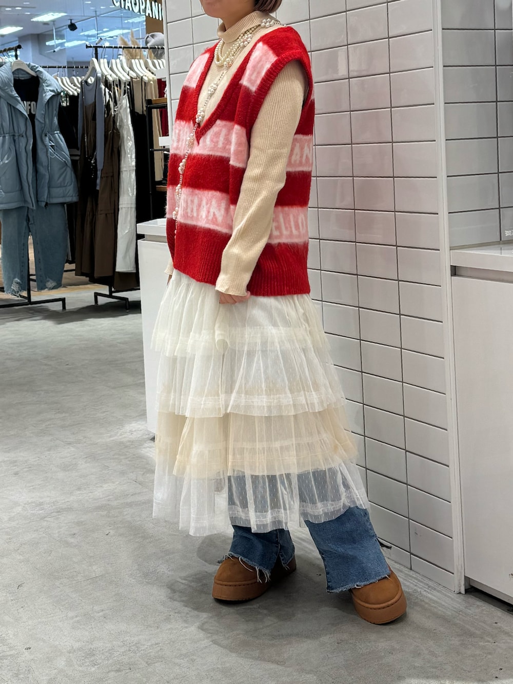 レッド系のベスト、ホワイト系のスカート、ブラウン系のサンダルを着用したレディースの秋コーディネートの2枚目の写真