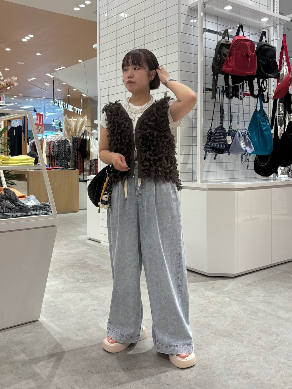 ホワイト系のサンダル、ブラウン系のベスト、ブルー系のデニムパンツを着用したレディースの夏コーディネートの2枚目の写真