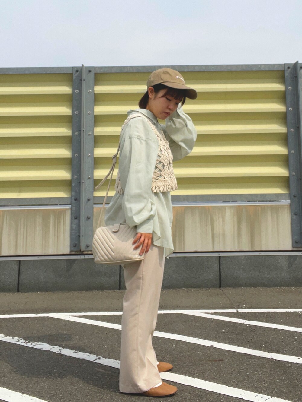 ベージュ系のスラックス、ベージュ系のベスト、ホワイト系のショルダーバッグを着用したレディースの春コーディネートの5枚目の写真