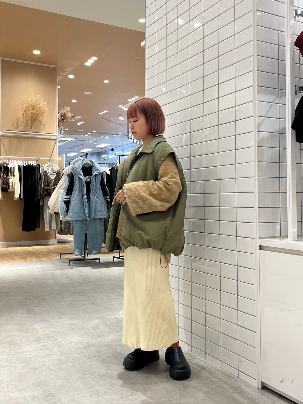 グリーン系のブルゾン、ホワイト系のスカート、ブラック系のブーツを着用したレディースの秋コーディネートの2枚目の写真