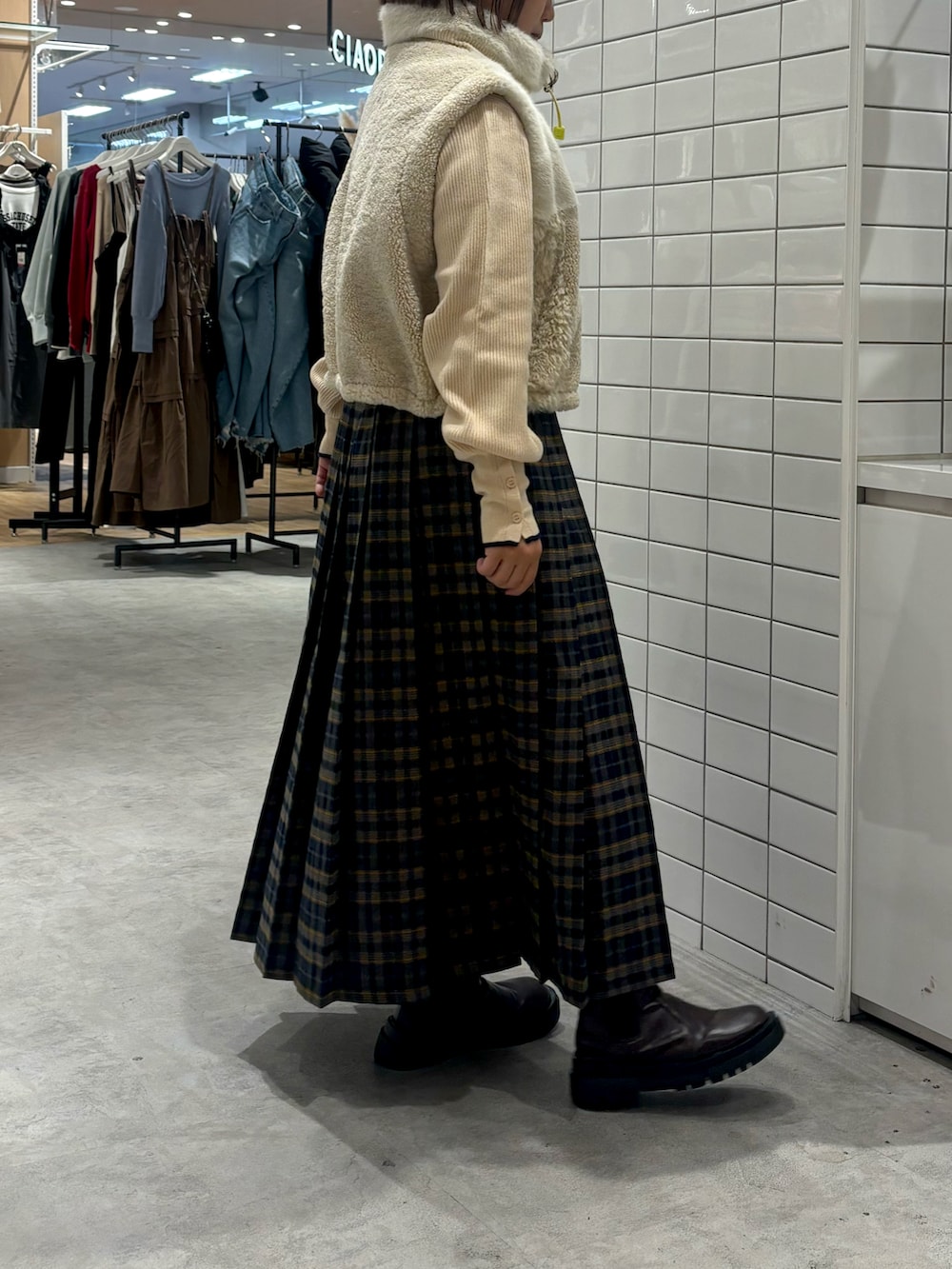 ブルー系のスカート、ブラウン系のブーツ、ホワイト系のベストを着用したレディースの秋コーディネートの2枚目の写真