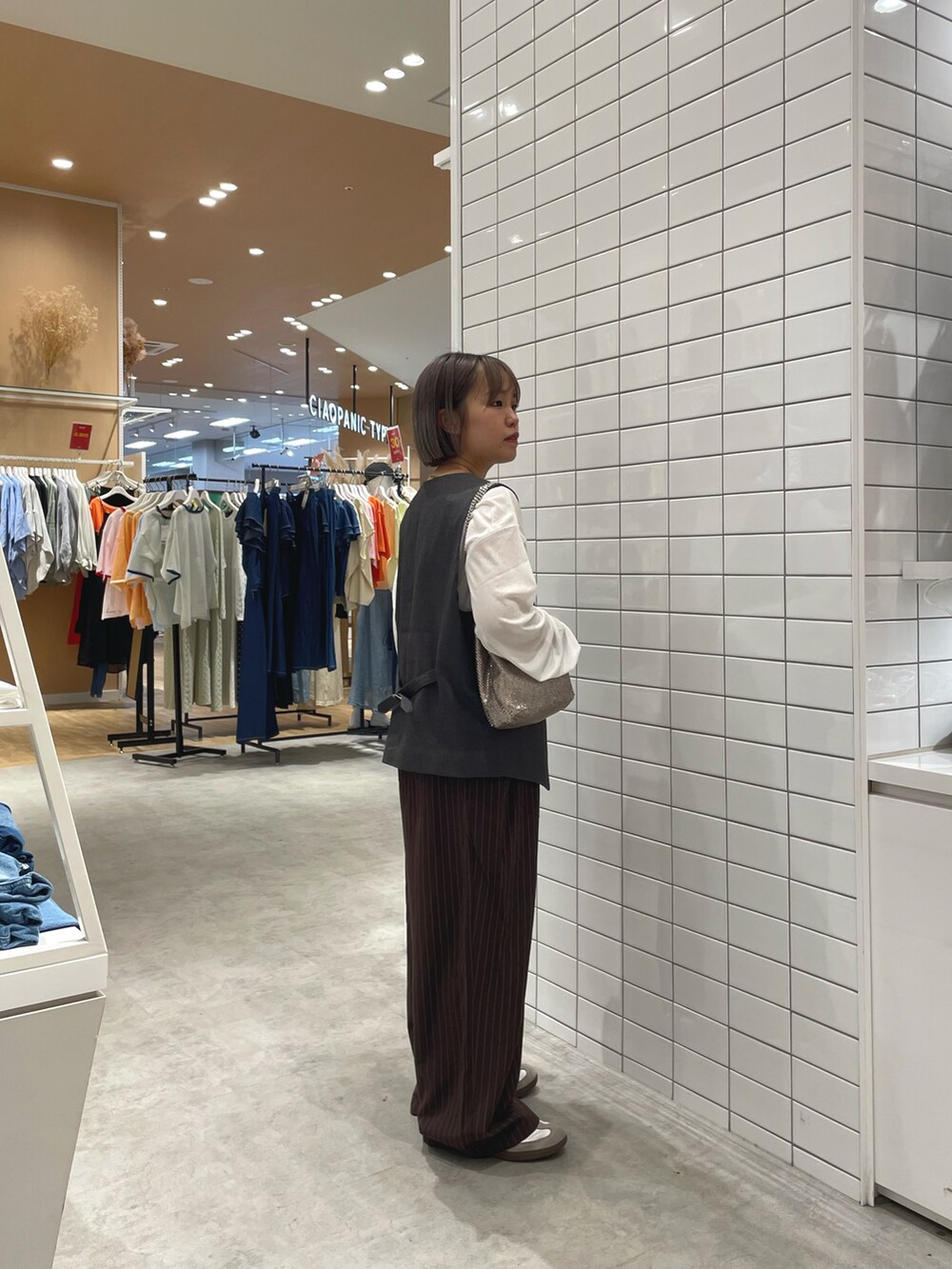 ゴールド系のショルダーバッグ、ブラウン系のスラックス、ホワイト系のTシャツ/カットソーを着用したレディースの秋コーディネートの3枚目の写真