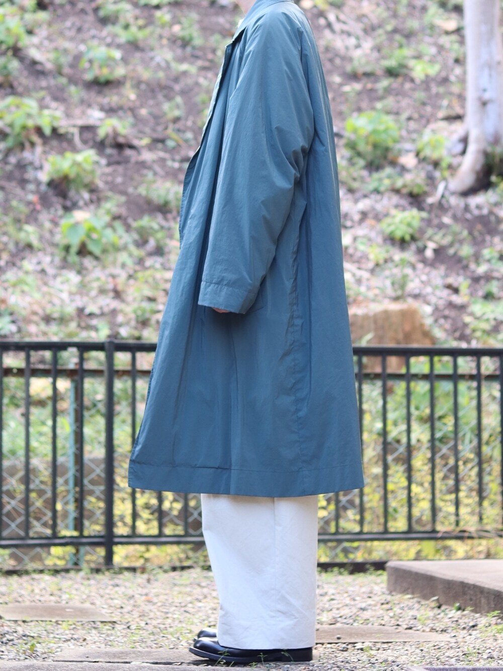 グレー系のニット/セーター、グリーン系のチェスターコート、ブラック系のショルダーバッグを着用したメンズの冬コーディネートの2枚目の写真