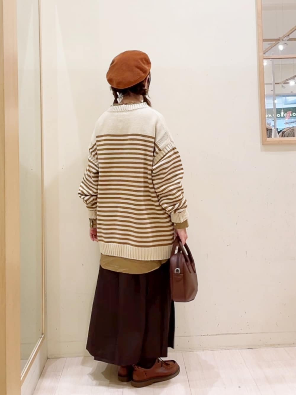 イエロー系のニット/セーター、ブラウン系のスカート、イエロー系のシャツ/ブラウスを着用したレディースの冬コーディネートの2枚目の写真