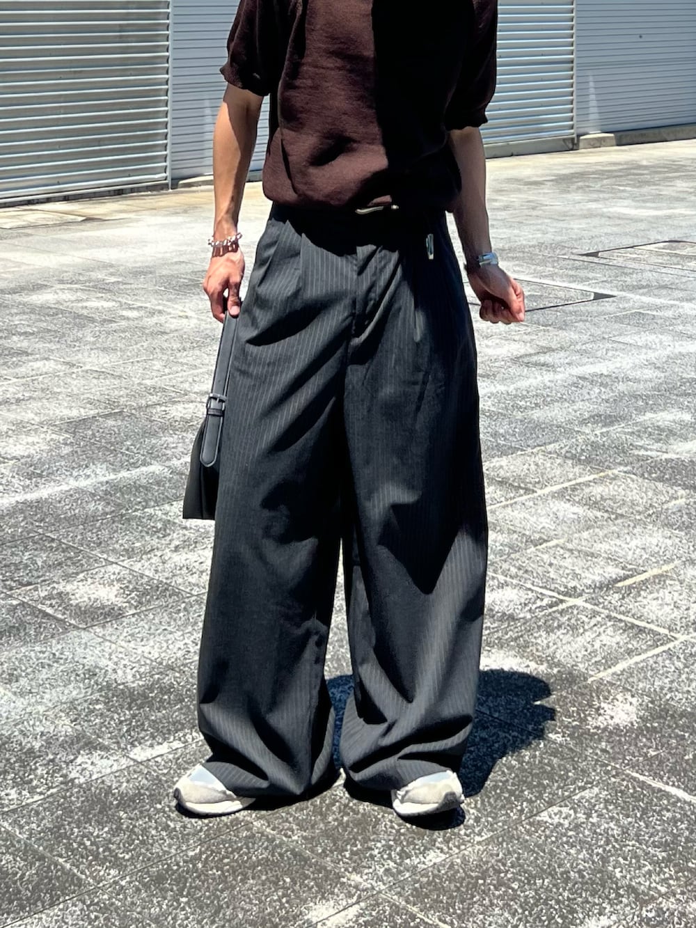 ブラック系のハンドバッグ、グレー系のスラックス、ブラウン系のポロシャツを着用したメンズの夏コーディネートの2枚目の写真