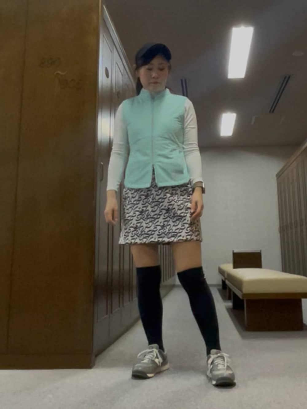 グレー系のスカート、グリーン系のベスト、ブラック系のサンバイザーを着用したレディースの春コーディネートの3枚目の写真