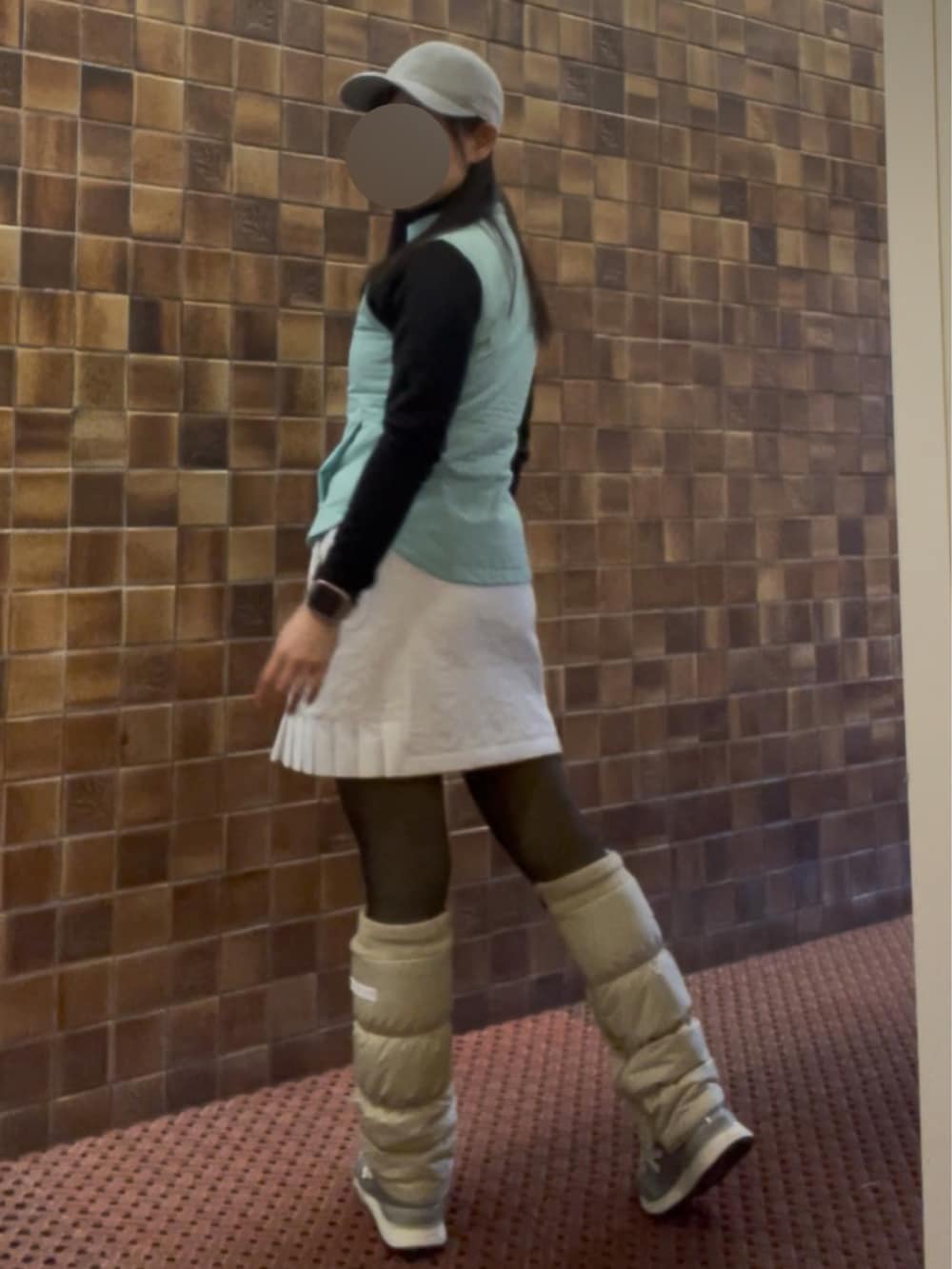 グリーン系のベスト、ホワイト系のスカート、シルバー系のキャップを着用したレディースの春コーディネートの2枚目の写真