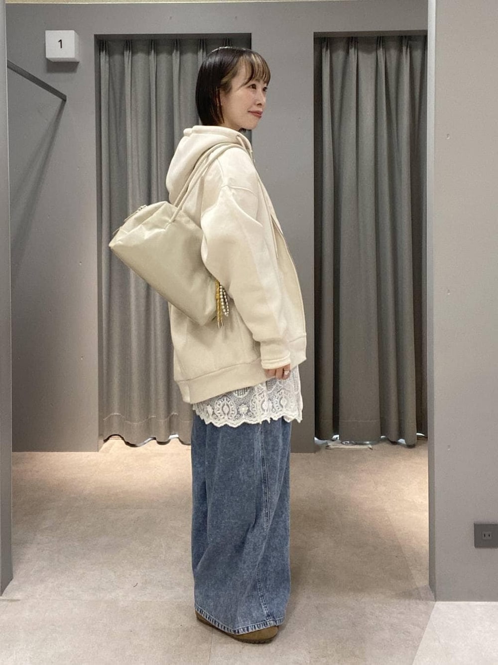 ホワイト系のパーカー、ブルー系のデニムパンツ、ホワイト系のボストンバッグを着用したレディースの春コーディネートの2枚目の写真