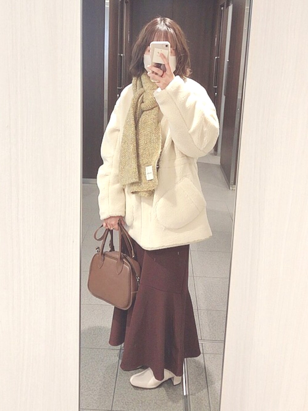 ホワイト系のムートンコート、ブラウン系のボストンバッグ、ブラウン系のスカートを着用したレディースの冬コーディネートの2枚目の写真