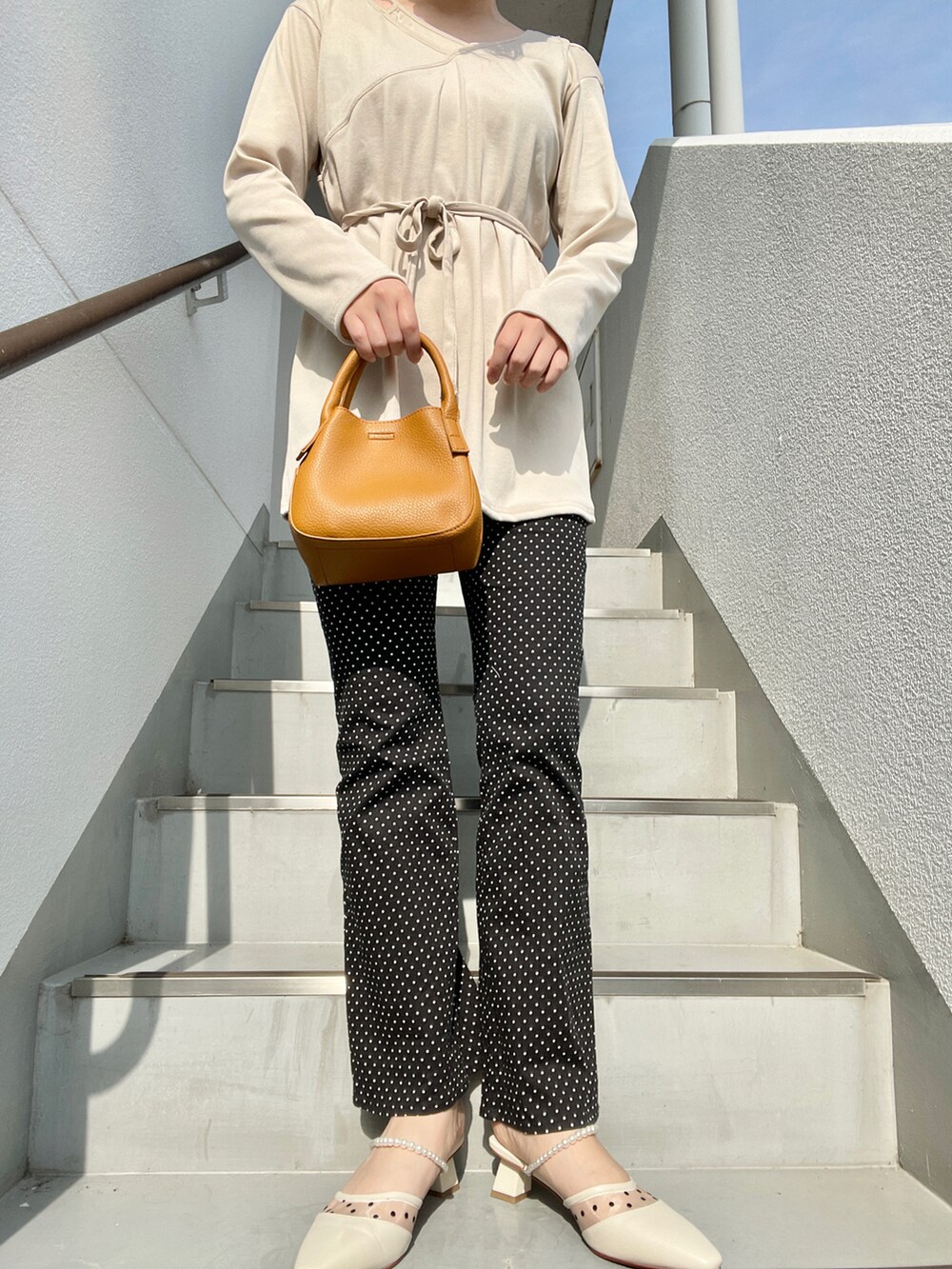 ブラウン系のハンドバッグ、ブラック系のその他パンツ、ホワイト系のパンプスを着用したレディースの春コーディネートの2枚目の写真