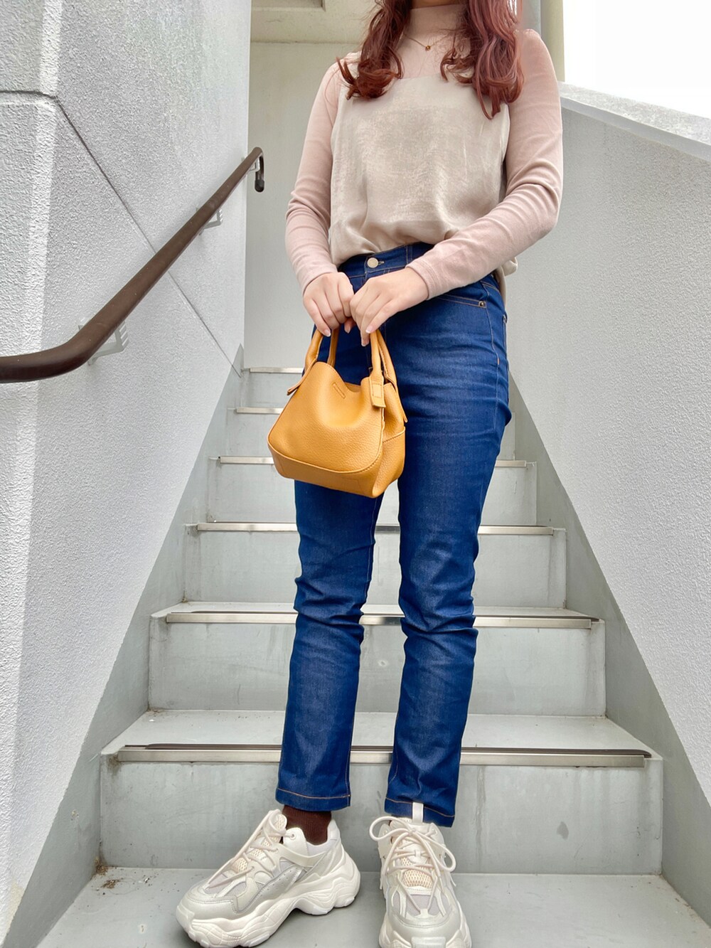 ブラウン系のハンドバッグ、ブルー系のデニムパンツ、ホワイト系のスニーカーを着用したレディースの春コーディネートの2枚目の写真