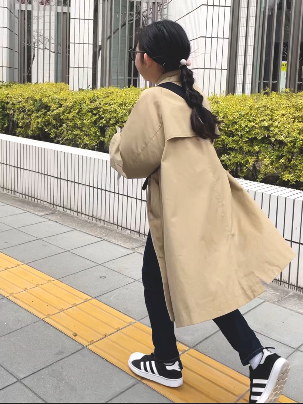 ブラック系のスニーカー、ブルー系のデニムパンツ、ベージュ系のトレンチコートを着用したキッズの春コーディネートの2枚目の写真