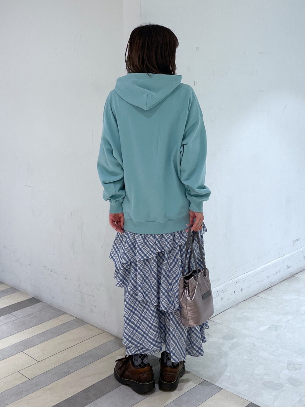 グリーン系のパーカー、ブルー系のスカート、シルバー系のショルダーバッグを着用したレディースの冬コーディネートの2枚目の写真