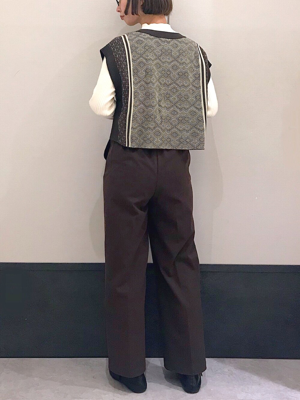 ブラウン系のベスト、ホワイト系のニット/セーター、ブラック系のショルダーバッグを着用したレディースの冬コーディネートの2枚目の写真