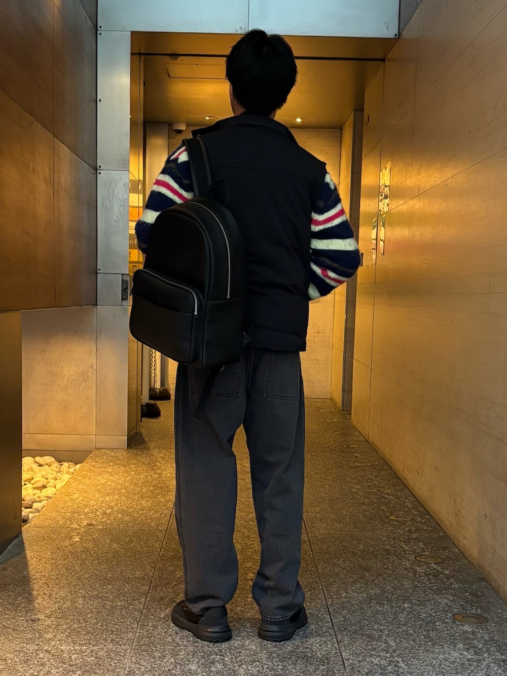 ブラック系のダウンベスト、ブルー系のカーディガン/ボレロ、ブラック系のデニムパンツを着用したメンズの冬コーディネートの3枚目の写真