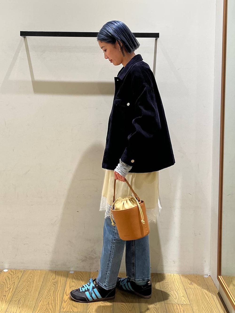 イエロー系のハンドバッグ、ブルー系のデニムパンツ、ベージュ系のワンピースを着用したレディースの冬コーディネートの2枚目の写真