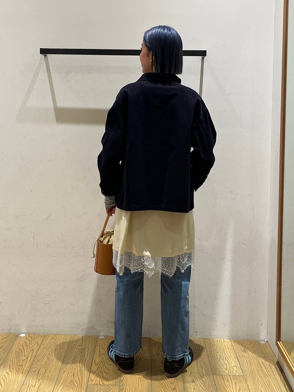 イエロー系のハンドバッグ、ブルー系のデニムパンツ、ベージュ系のワンピースを着用したレディースの冬コーディネートの4枚目の写真