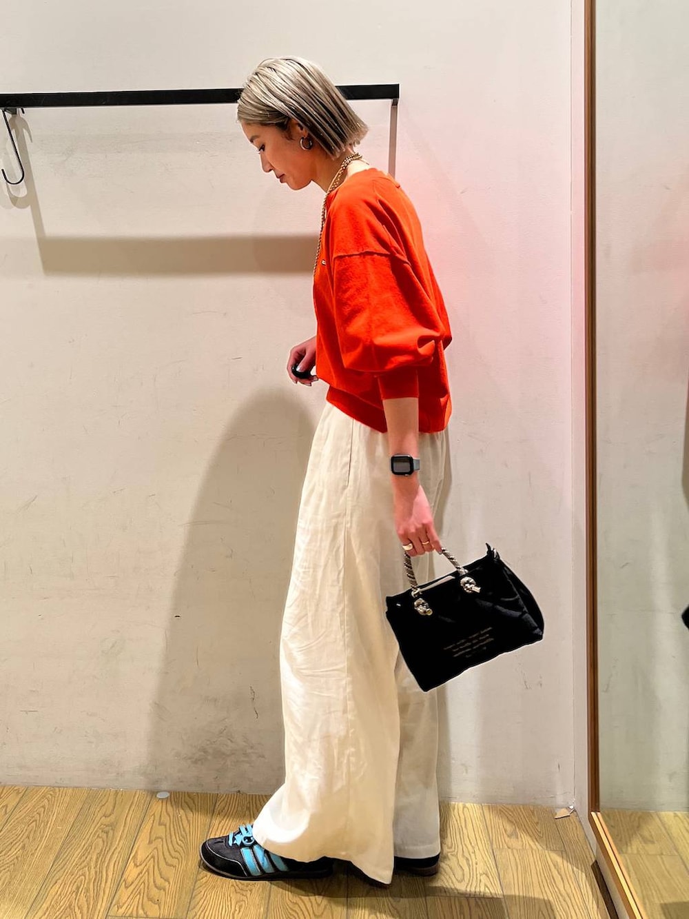 ベージュ系のその他パンツ、オレンジ系のニット/セーター、ブラック系のショルダーバッグを着用したレディースの春コーディネートの2枚目の写真