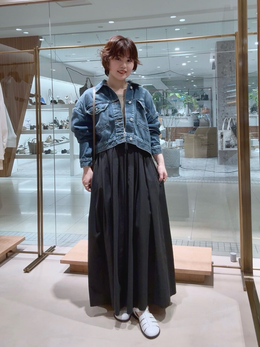ブルー系のデニムジャケット、ベージュ系のニット/セーター、ブラック系のスカートを着用したレディースの春コーディネートの2枚目の写真