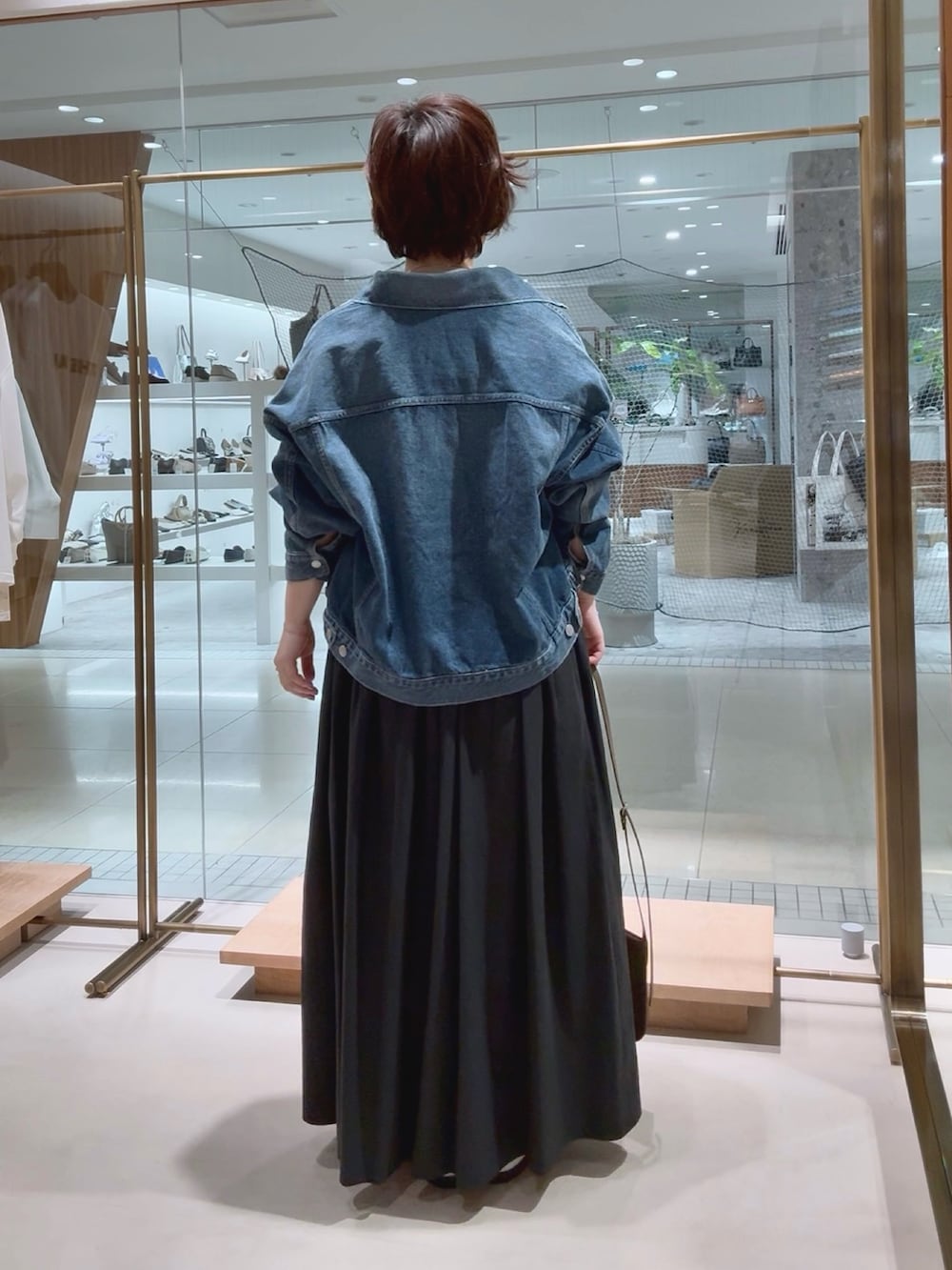 ブルー系のデニムジャケット、ベージュ系のニット/セーター、ブラック系のスカートを着用したレディースの春コーディネートの4枚目の写真