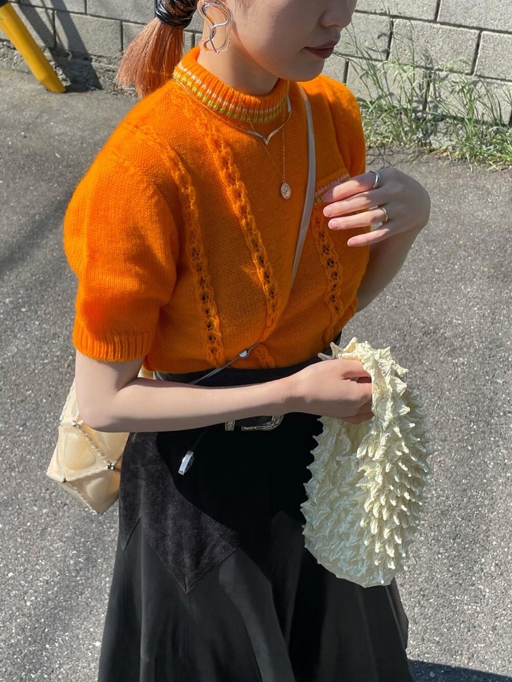 オレンジ系のニット/セーター、ブラック系のスカート、ベージュ系のショルダーバッグを着用したレディースの春コーディネートの2枚目の写真