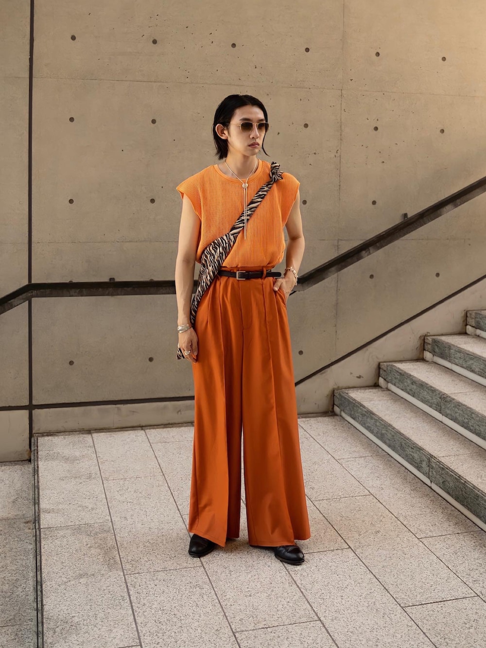 オレンジ系のTシャツ/カットソー、オレンジ系のスラックス、ブラック系のブーツを着用したメンズの夏コーディネートの2枚目の写真