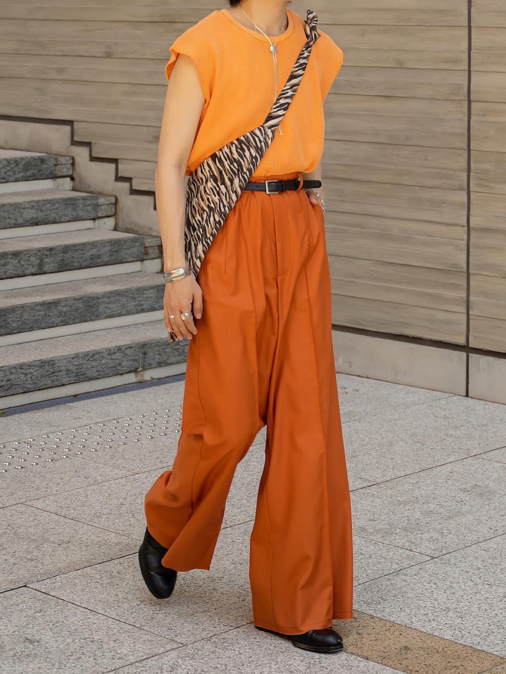 オレンジ系のTシャツ/カットソー、オレンジ系のスラックス、ブラック系のブーツを着用したメンズの夏コーディネートの3枚目の写真